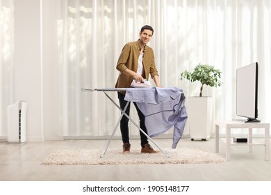 Young man ironing a shirt at home in a living room