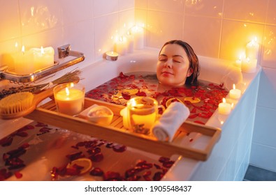 Jonge vrouw geniet van spirituele aura reiniging rozenbloem bad met rozenblaadjes en kaarsen tijdens volle maan ritueel. Lichaamsverzorging en mentale gezondheid routine.