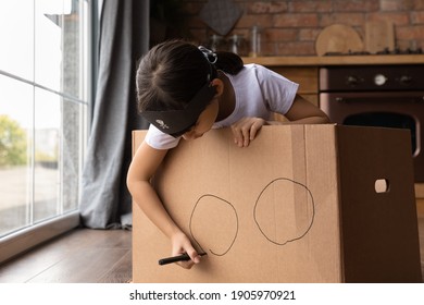 Close up cute little girl playing funny game, pretending pirate, adorable child kid wearing handmade costume, bandana with skull, drawing on cardboard box, ship, having fun in kitchen at home