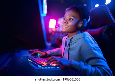 Professional Streamer African young woman cyber gamer studio room with personal computer armchair, keyboard in neon color blur background.