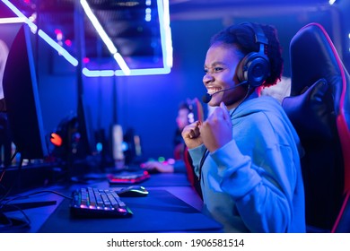 Young American African smile woman professional gamer win in online video game with headphones, neon background.