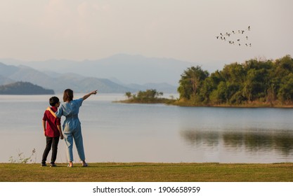 madre e hijo parados al lado de un gran lago y ven la vista de la montaña en el fondo, mamá señalando con el dedo a los pájaros que vuelan en el cielo. Idea para viajes turísticos familiares juntos.