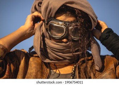 Post-apocalyptic woman portrait outdoors. Young slim girl warrior in shabby clothes standing in a confident pose looking down. Nuclear post-apocalypse time. Life after doomsday concept. Desert and