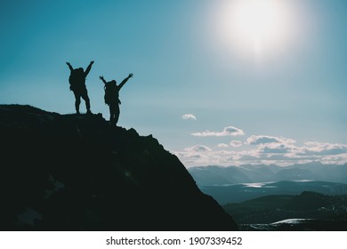Silhouetten van twee gelukkige wandelaars in winnaarshoudingen met opgeheven armen staan ​​op de bergtop