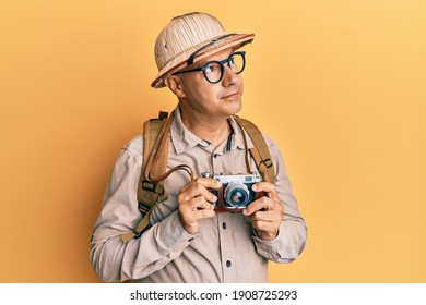 Kaşif şapkası ve eski fotoğraf makinesi takan orta yaşlı kel adam gülümseyerek yana bakıyor ve düşünüyor.