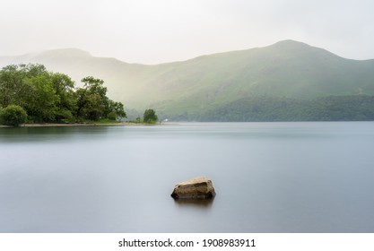 Sunrise on Derwent Water in the Lake District National Park, Cumbria England.  The sun is shining on the trees in the midground and the moring mist is lighting out Cat Bells in the background.