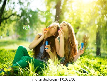 Beauty teen girls having fun outdoors. Beautiful joyful teenagers laughing and blowing soap bubbles in spring park. Girlfriends outdoor. 