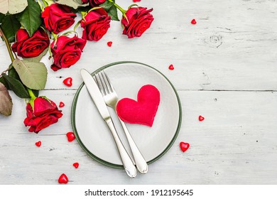 Romantischer Esstisch. Liebeskonzept für Valentinstag oder Muttertag, Hochzeitsbesteck. Blumenstrauß aus frischen Burgunder-Rosen, weißer Vintage-Holzbretter-Hintergrund, Draufsicht