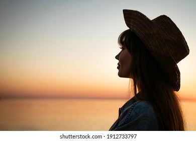Portrait of a young woman by the sea in a hat at sunset