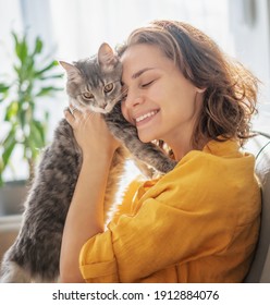 Retrato de primer plano de una hermosa joven alegre con un lindo gato gris en sus brazos en casa en el sofá