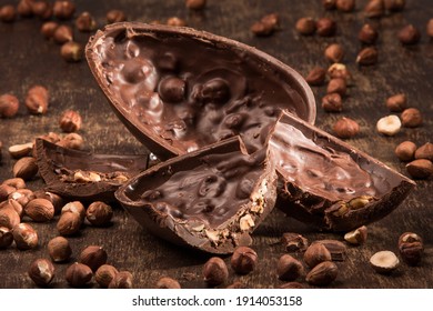 Gefülltes Schokoladen-Osterei auf einem Holztisch mit Haselnüssen.