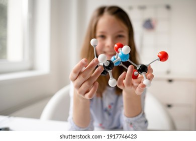 uma linda colegial loira está aprendendo química com a ajuda de um modelo de molécula e está sentada à mesa