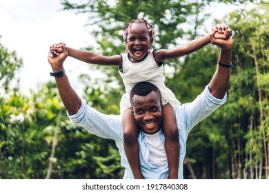 幸せな愛を楽しむ黒人家族アフリカ系アメリカ人の父親の肖像画は、娘を運ぶアフリカ系アメリカ人の小さな女の子の子供の笑顔と楽しい瞬間を自宅の夏の公園で楽しい時間を過ごしています