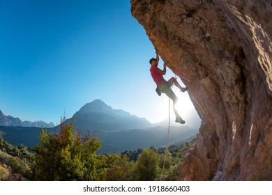 Atletische man klimt een overhangende rots met touw, loodklimmen. silhouet van een bergbeklimmer op een bergachtergrond. buitensport en recreatie