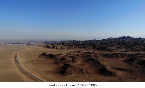乾燥した砂漠の山の近くの砂利道を走る車。ドローンからの空撮は、道路と山を空にします。未舗装の道路がある広大な砂漠の風景。クレイ山脈