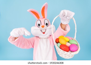 Osterhase oder Hase oder Hase mit Korb mit farbigen Eiern, zeigt Daumenfinger nach oben, hat Spaß, tanzt, feiert fröhliche ostern. Osterhase isoliert auf blauem Hintergrund