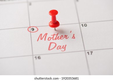 Glückliches Muttertagskonzept. Zugeschnittenes Nahaufnahmefoto der roten Stecknadel, die am Kalender mit der Aufschrift Muttertag befestigt ist