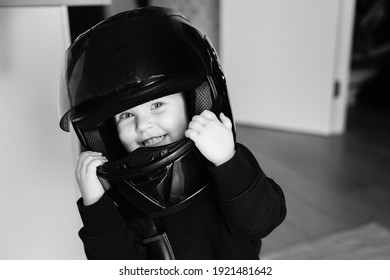 頭にオートバイのヘルメットをかぶった小さなかわいい女の子がゲームをプレイし、美しい目でカメラに微笑みかけます。白黒写真