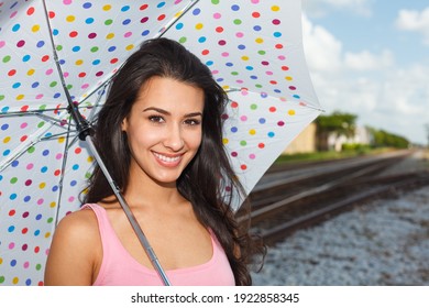 Pretty young woman outdoors with a polka dot umbrella by a railroad track.