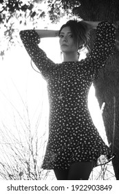 Foto en blanco y negro de hermosa mujer con una hermosa chica morena con un vestido casual levantando los brazos hasta el cabello en un fondo quemado con luz solar blanca debajo de un árbol en el parque en un tiroteo