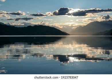 Ein Sonnenuntergang am Millstätter See in Österreich. Der See ist von hohen Alpen umgeben. Ruhige Oberfläche des Sees, die die Sonnenstrahlen reflektiert. Die Sonne geht hinter den Bergen unter. Etwas bewölkt. Natürliche Schönheit
