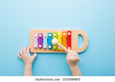 Baby hand holding hammer and playing colorful xylophone on light blue table background. Closeup. Music toy instrument of development for little kids. Point of view shot.