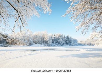 Bevroren rivier in een kader van met sneeuw bedekte bomen, rijp op takken. Helder blauwe lucht. Idyllisch landschap. Winter Wonderland. Natuur, seizoenen, klimaatverandering, ecologie, ecotoerisme, kerstvakanties