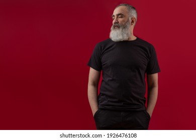 黒の t シャツを着ている灰色のひげを持つ大人のハンサムなシニア男性モデル。正面図。濃い赤の背景にロゴやデザイン用のスペースをモックアップします