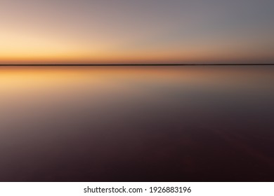 Tranquil minimalist landscape with smooth surface of the pink salt lake with calm water with horizon with clear sky in sunset time. Simple beautiful natural calm background