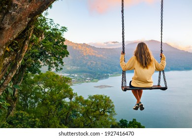 夏休み。若い女性は、熱帯の湖の上の高い崖の上の木のロープ ブランコに座る。素晴らしいジャングルの景色を見て幸せな女の子。ブヤン湖は、インドネシアのバリ島で人気のある旅行先です。
