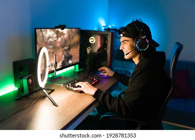Glimlachende jongeman die zijn online videogame live streamt met een smartphone en een ringlicht. Blije gamer klaar om te beginnen met spelen op een spelcomputer