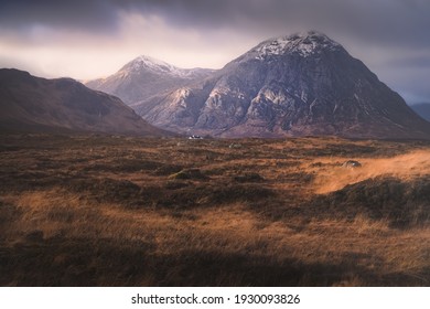 スコットランド、スコットランドのスコットランド高地のグレンコーにある、遠く離れたブラックロック コテージを持つブアチャイユ エティブ モーの暗い、不機嫌な山の風景にドラマチックな黄金の光。