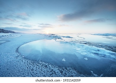 Orilla del mar Báltico congelada al atardecer. Primer plano de fragmentos de hielo, bosque de pinos cubierto de nieve en el fondo. Paisaje nublado colorido. Reflexiones de simetría en el agua. Naturaleza, cambio climático. Vista panorámica