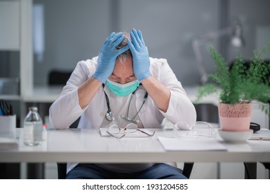 An elderly medic is saddened by the large number of deaths from covid-19, he is sad and holds his hands to his face.