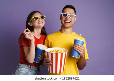 Pareja alegre en gafas 3d comiendo palomitas de maíz mientras ve una película aislada sobre fondo violeta