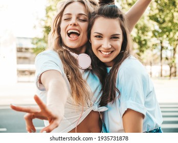 トレンディな夏の白い t シャツの服で 2 つの若い美しい笑顔流行に敏感な女性の肖像画。セクシーな屈託のない女性が通りの背景にポーズします。楽しんで、ハグして、夢中になるポジティブなモデル