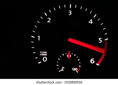 Izbliza tahometar na kontrolnoj ploči automobila na crnom tlu. 5000 - 6000 okretaja u minuti.