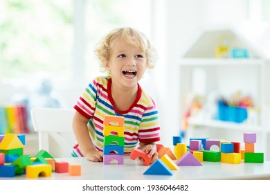 Fëmijë duke luajtur me blloqe lodrash shumëngjyrëshe. Djalë i vogël duke ndërtuar kullë me lodra blloqesh. Lodra dhe lojëra edukative dhe krijuese për fëmijë të vegjël. Foshnje në dhomë gjumi të bardhë me tulla ylberi. Fëmijë në shtëpi.