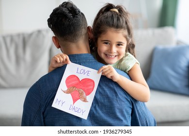 Vatertagskonzept. Lächelndes kleines Mädchen, das Papa umarmt und eine Grußkarte hält