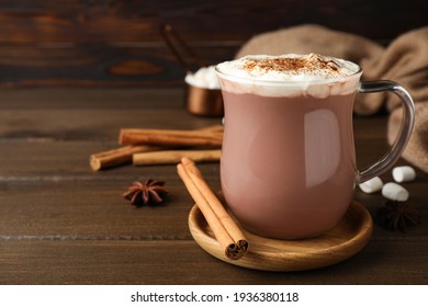 Secangkir cokelat panas dengan krim kocok dan kayu manis aromatik di atas meja kayu. Ruang untuk teks