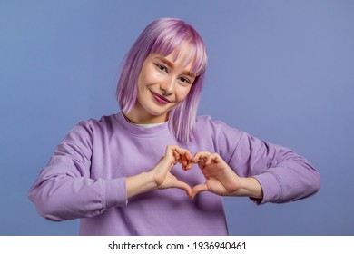 Aardige mooie vrouw die een hartvormig teken maakt bij haar borst. Violet geverfd haar. Paarse achtergrond. Vrouwengezondheid, vrijwilligerswerk, donatiehulp en liefdesconcept.