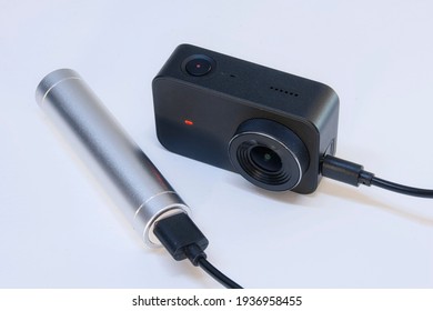 Een compacte action camera voor het maken van video en foto's op een witte achtergrond wordt opgeladen via een powerbank