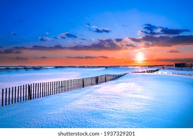 Adegan musim dingin di bawah langit berwarna saat matahari terbenam di pantai yang tertutup salju. Taman Negara Bagian Pantai Jones., Long Island NY