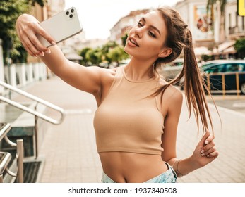 夏のカジュアルな服装で美しい笑顔のモデル。セクシーなのんきな女性がサングラスの通りでポーズします。スマート フォンで自分撮りセルフ ポートレート写真を撮る