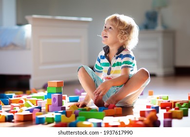 Kind spielt mit bunten Bauklötzen. Kinderspiel. Kleiner Junge baut Turm aus Blockspielzeug auf dunklem Boden in sonnigem weißem Schlafzimmer. Lernspiel für Baby und Kleinkind. Kinder bauen Spielzeughaus