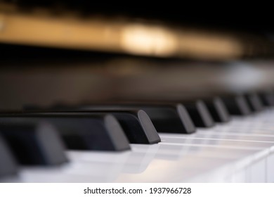 Close side view of shiny black and white piano keys with the reflection of the golden brass edge from low angle with shallow depth of field. Focus on the fourth black key from the center left