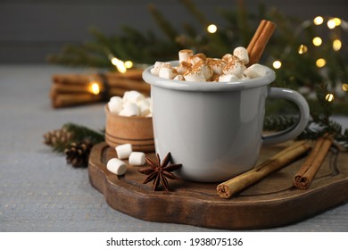 Secangkir minuman panas dengan kayu manis aromatik dan marshmallow di atas meja kayu abu-abu dengan lampu buram