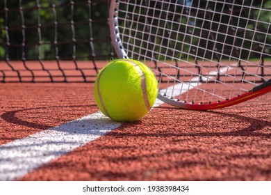 Pelota de tenis, línea y raqueta en una cancha al aire libre con la raqueta parada al final proyectando una sombra sobre la superficie para todo clima