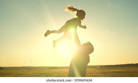 Dad tosses a happy child up into the sky at sunset. Daddy s daughter flies in his arms soaring in the air playing the game plane in the glare of the sun. The little kid rejoices with his father at