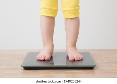 Bé gái đi chân trần đứng trên cân trên sàn gỗ ở nền tường màu xám nhạt. Cận cảnh. Khung cảnh phía trước. Quan tâm đến cơ thể. Khái niệm kiểm soát cân nặng.